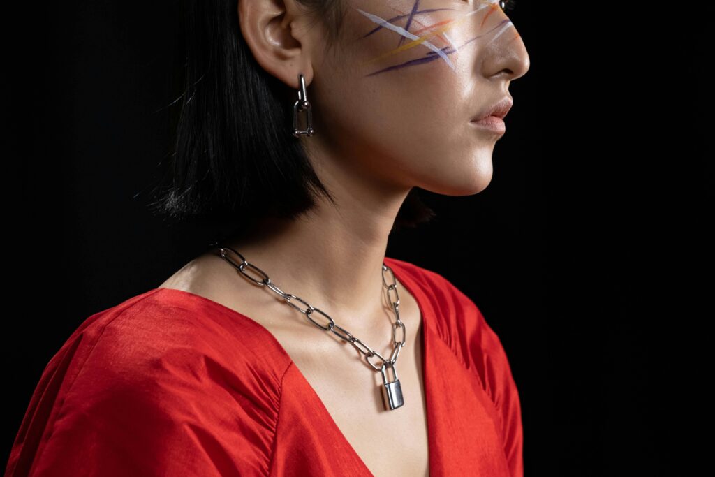 Artistic side profile portrait of a woman with face paint and bold jewelry on a black background.